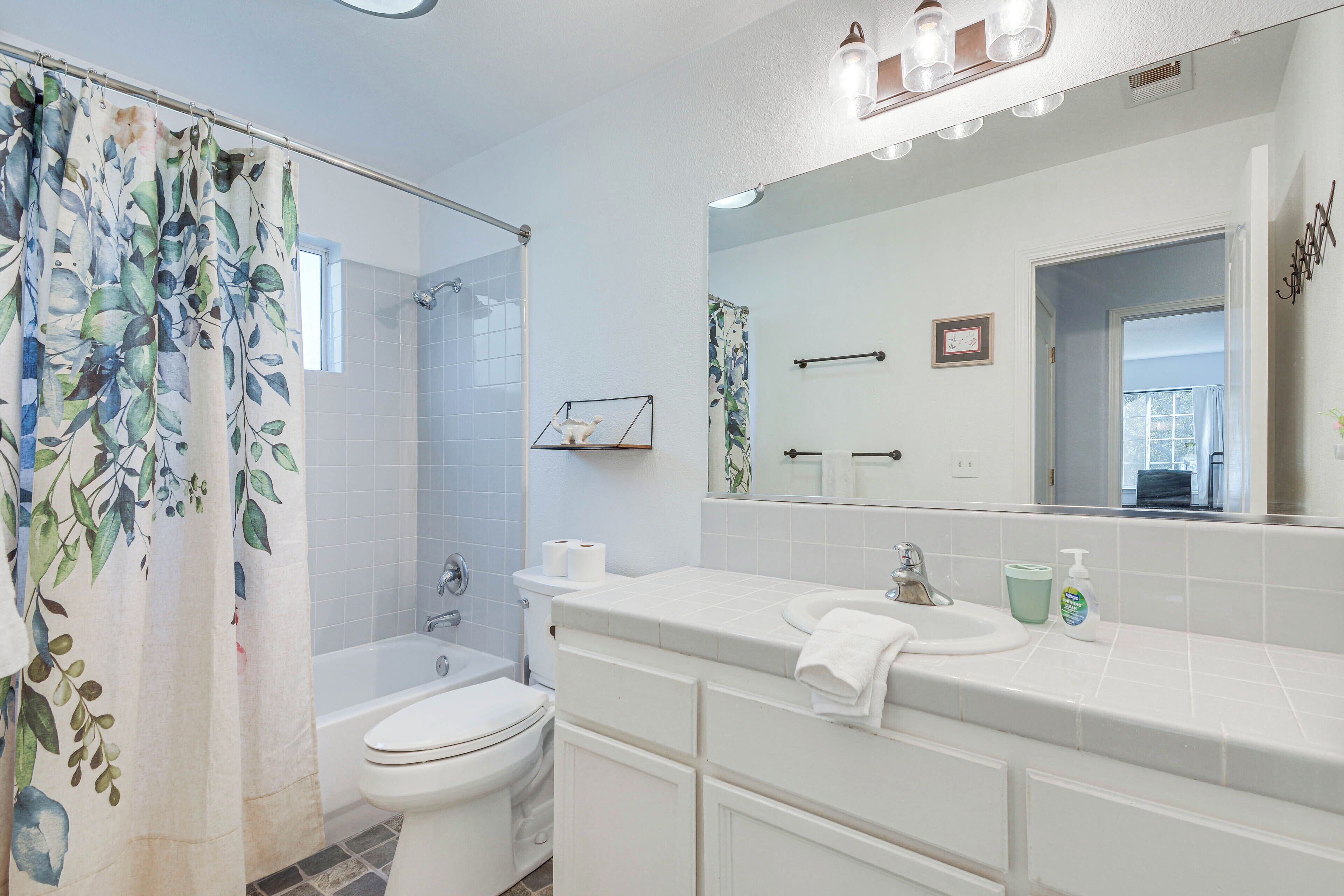 A bathroom with a shower curtain, toilet, sink, and mirror.