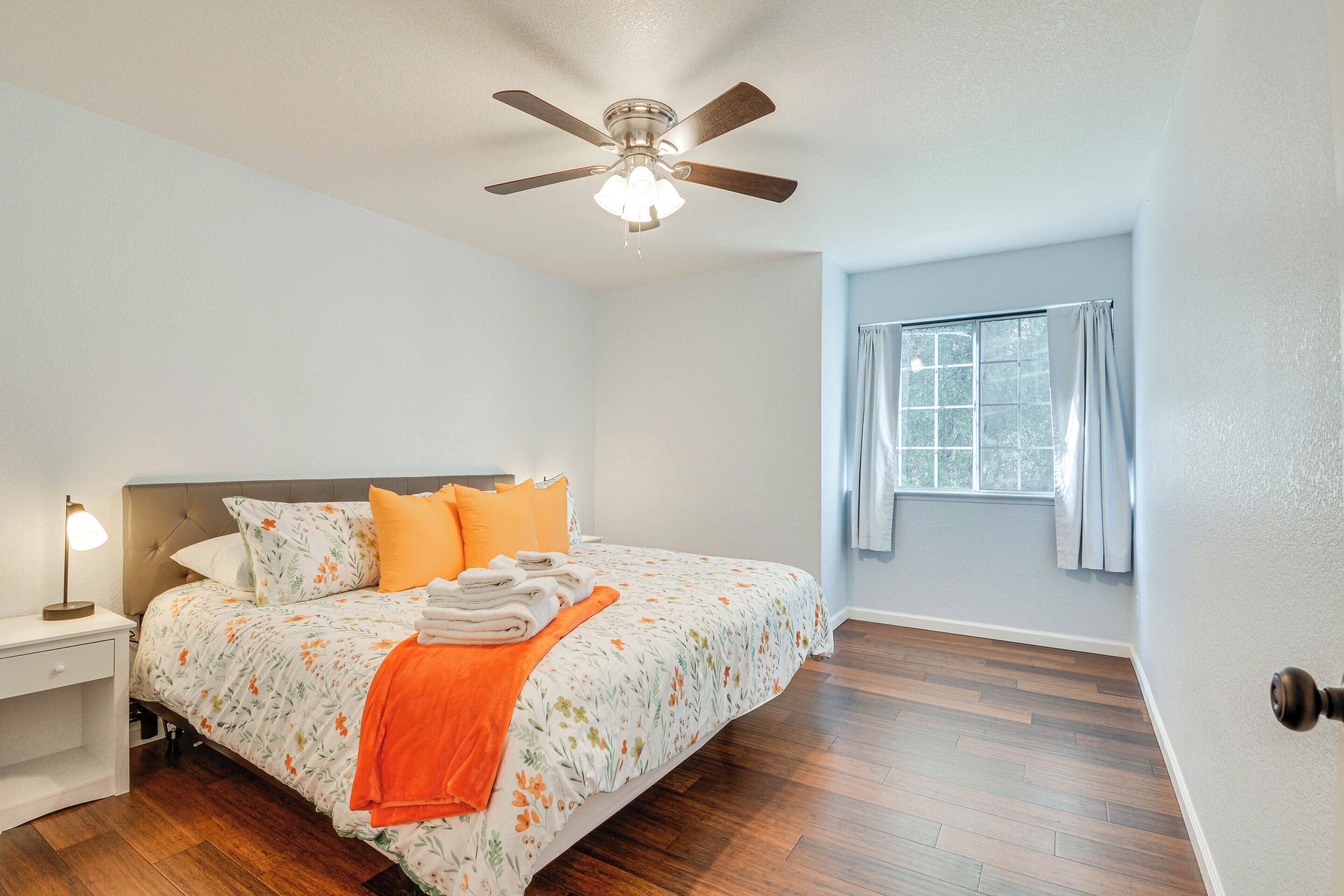A bedroom with a bed, a nightstand, a ceiling fan, and a window with curtains.