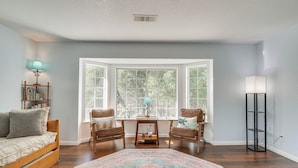 A room with a wooden bed, two chairs, a small table, and a large bay window with a view of trees. - Bright + Cozy Mariposa Getaway: 46 Mi to Yosemite! (Mariposa)