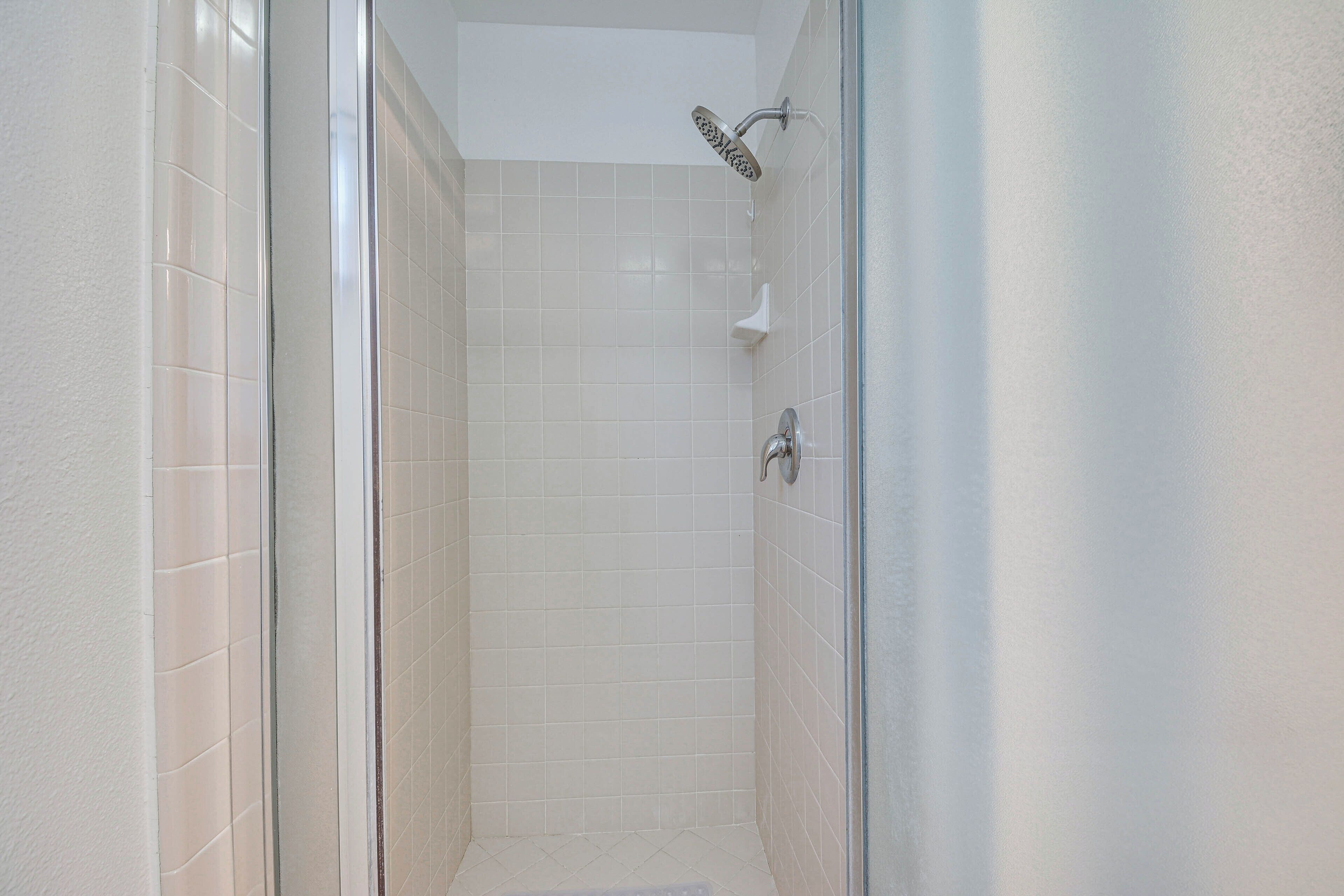 A small, enclosed shower area with white tiles and a glass door.