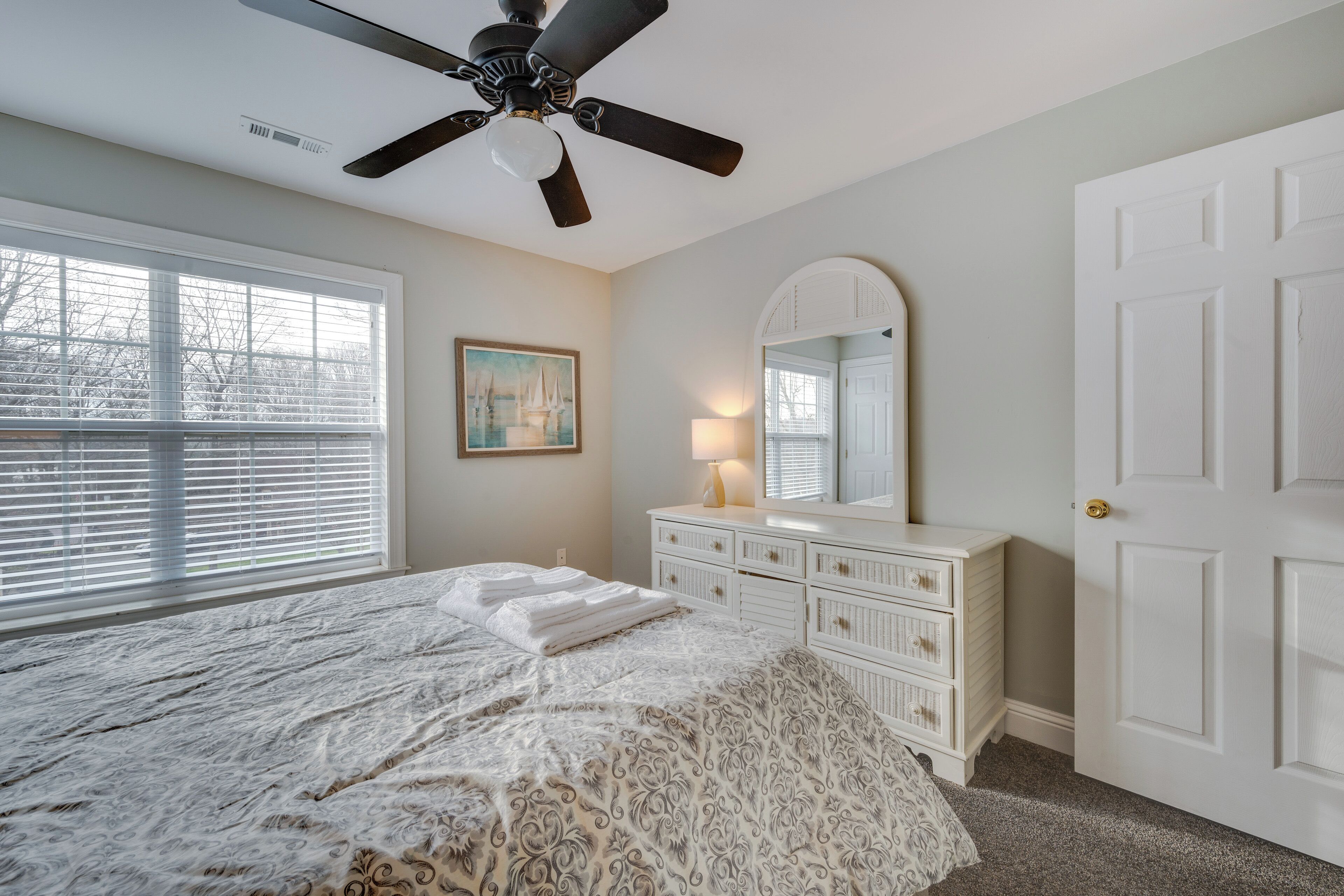 A bedroom with a bed, dresser, ceiling fan, and a window with blinds.