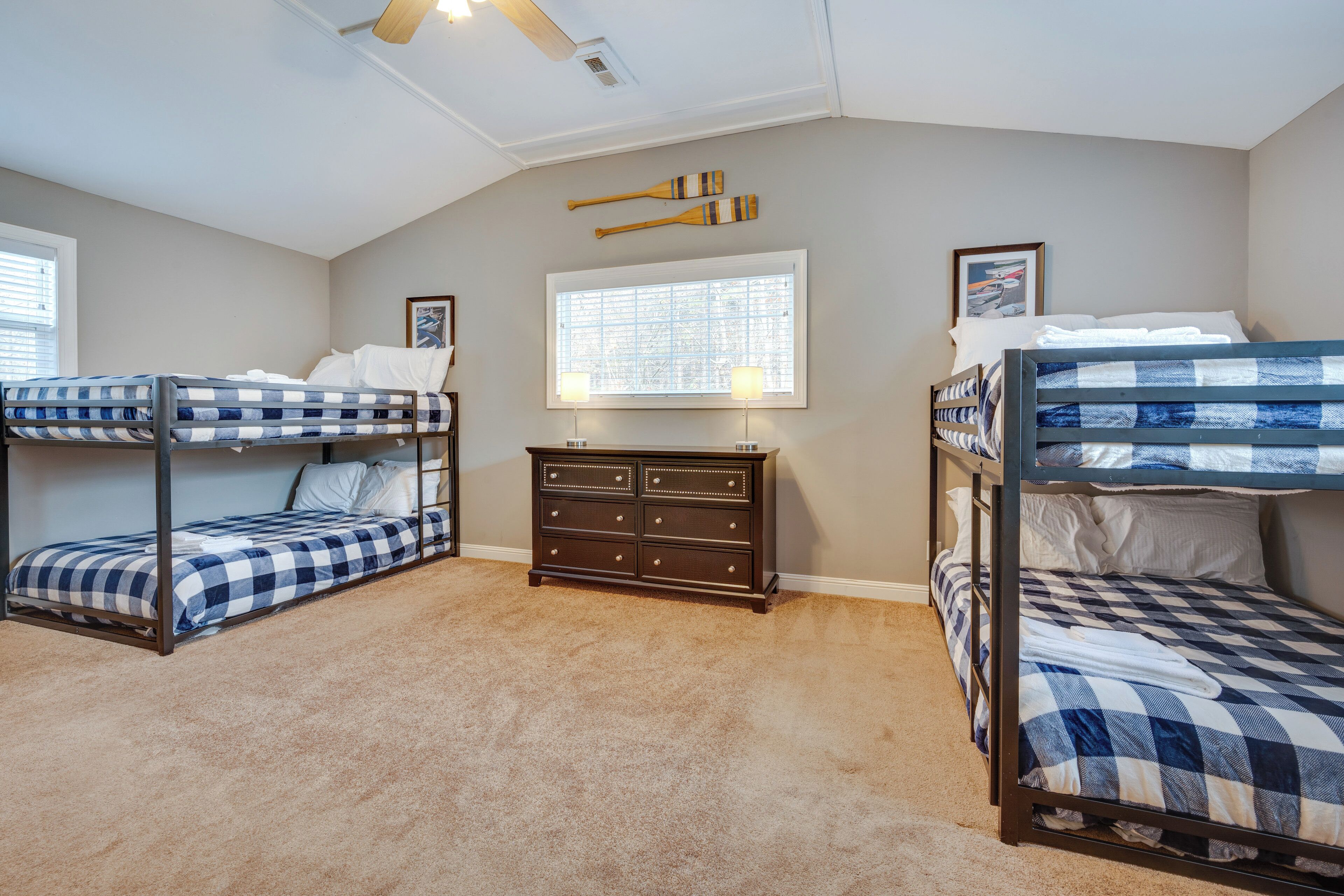 A bedroom with two bunk beds, a dresser, a window with blinds, and a ceiling fan.