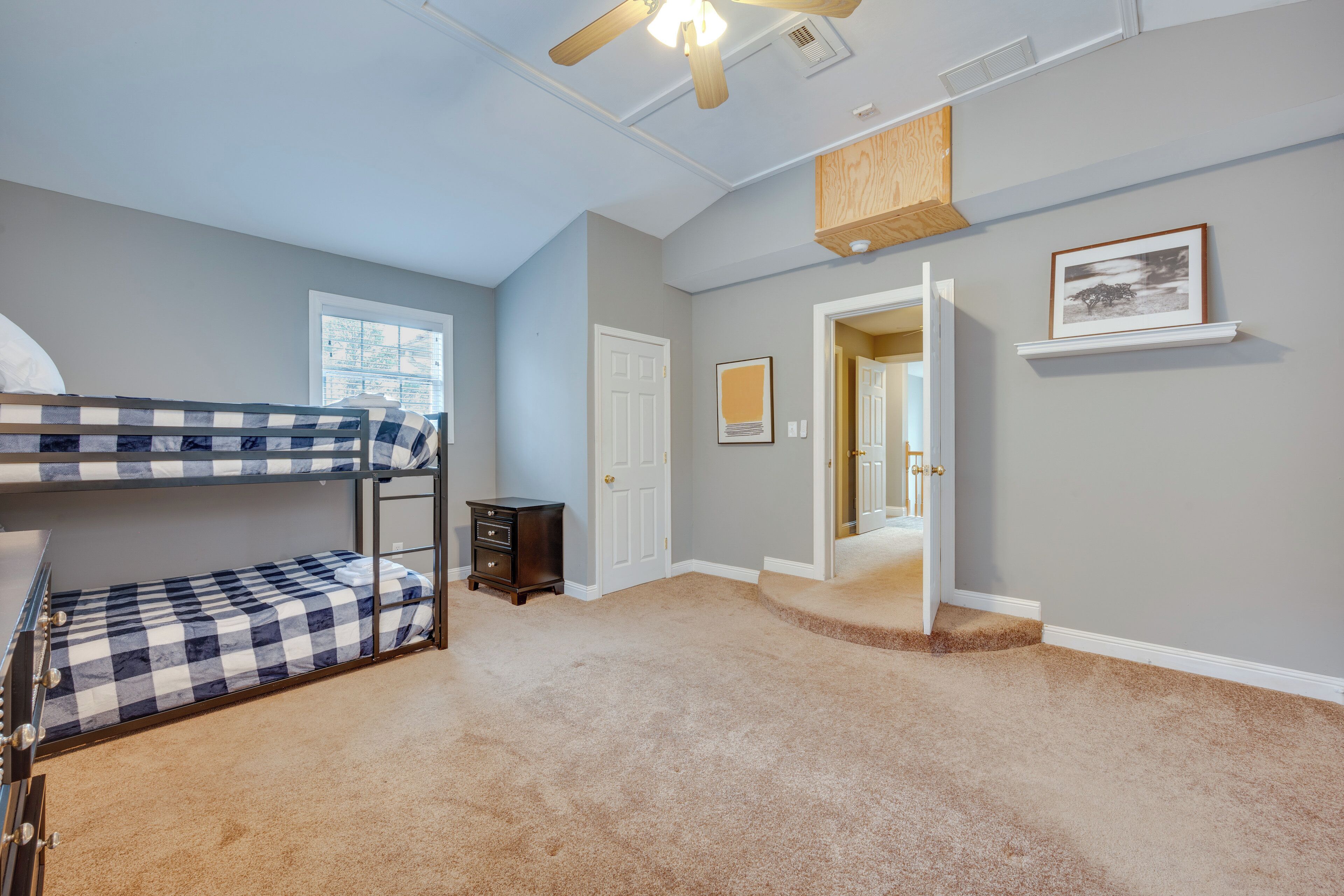 Une chambre avec un lit superposé, une commode, une porte et un couloir menant à une autre pièce.