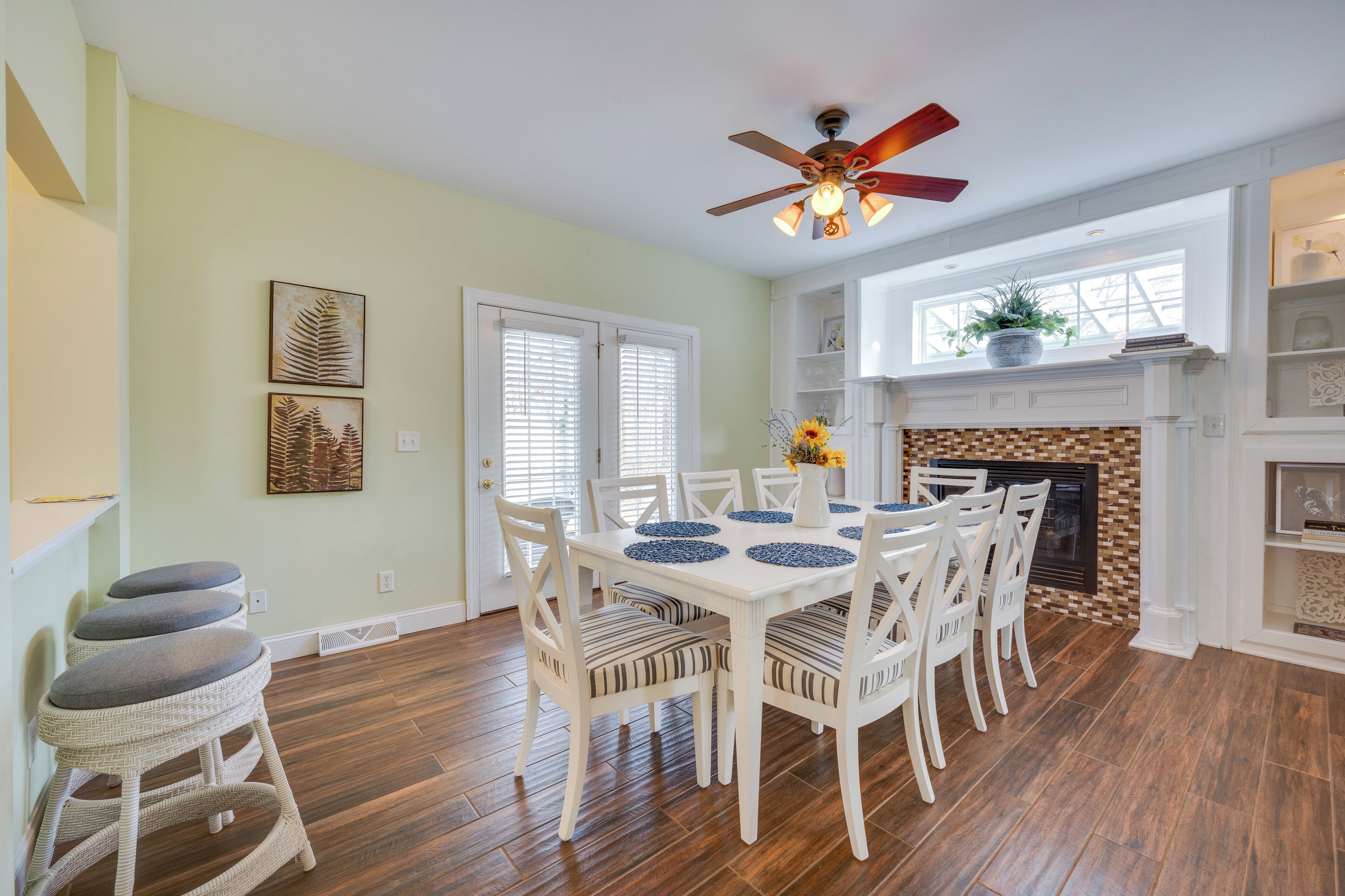 A dining area with a white table and chairs, a ceiling fan, and a fireplace.