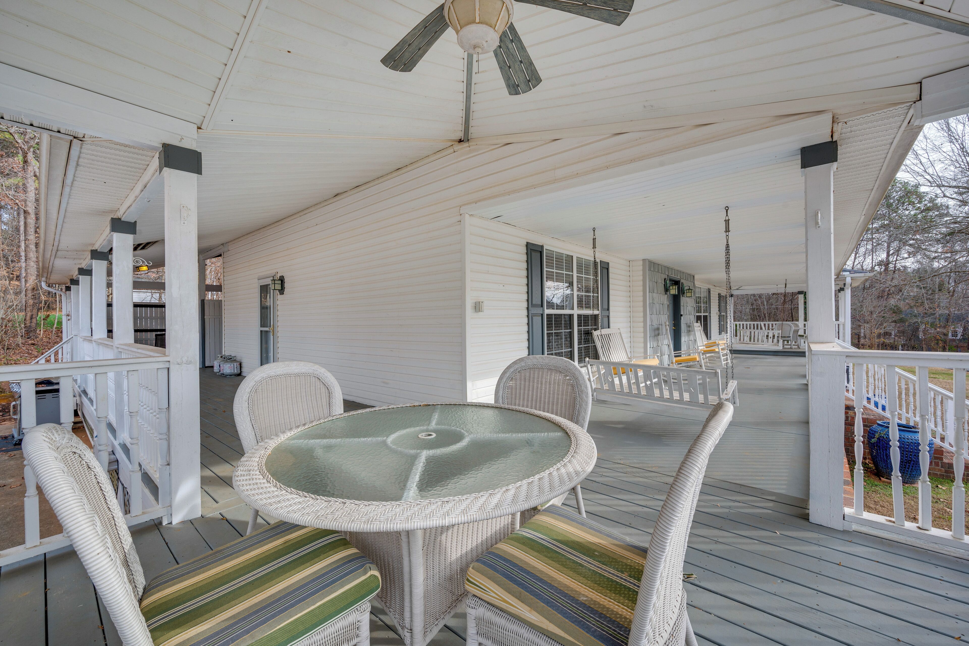 A covered porch with wicker furniture and a glass table, white railings, and a ceiling fan.