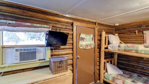 A cabin with bunk beds, a television, a window with curtains, and a wooden desk with a basket. - Black Diamond Guest Ranch Cabin w/ Lodge Access! (De Borgia)