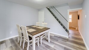 A dining area with a wooden table and white chairs, a staircase, and a hallway leading to another room.
