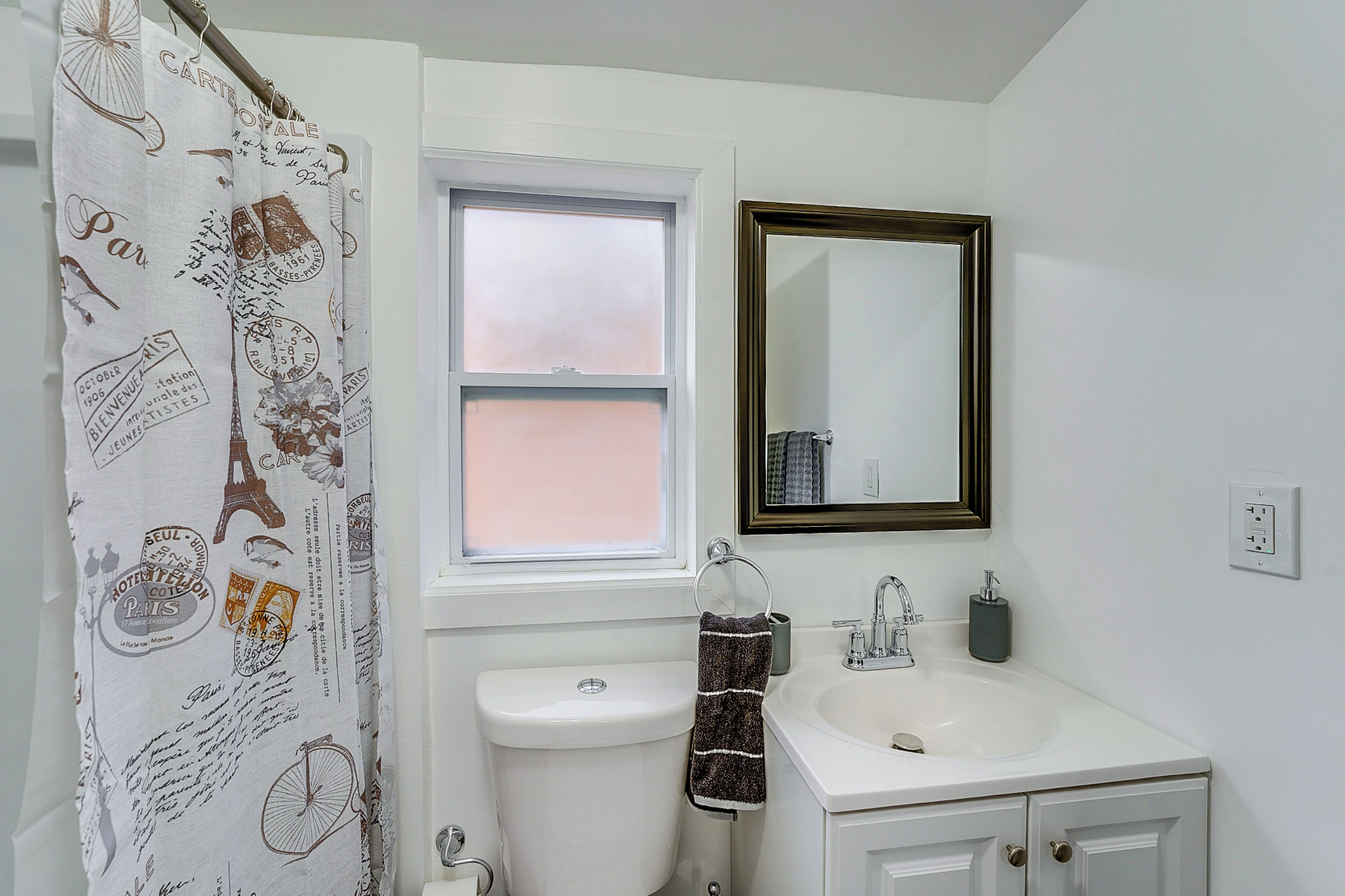 A bathroom with a white toilet, a sink, a mirror, and a shower curtain with Paris-themed designs.