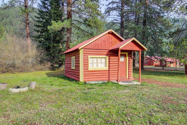 A small, single-story log cabin with a red roof and yellow trim, surrounded by a forested area. - Black Diamond Guest Ranch Studio: Hike & Fish (De Borgia)