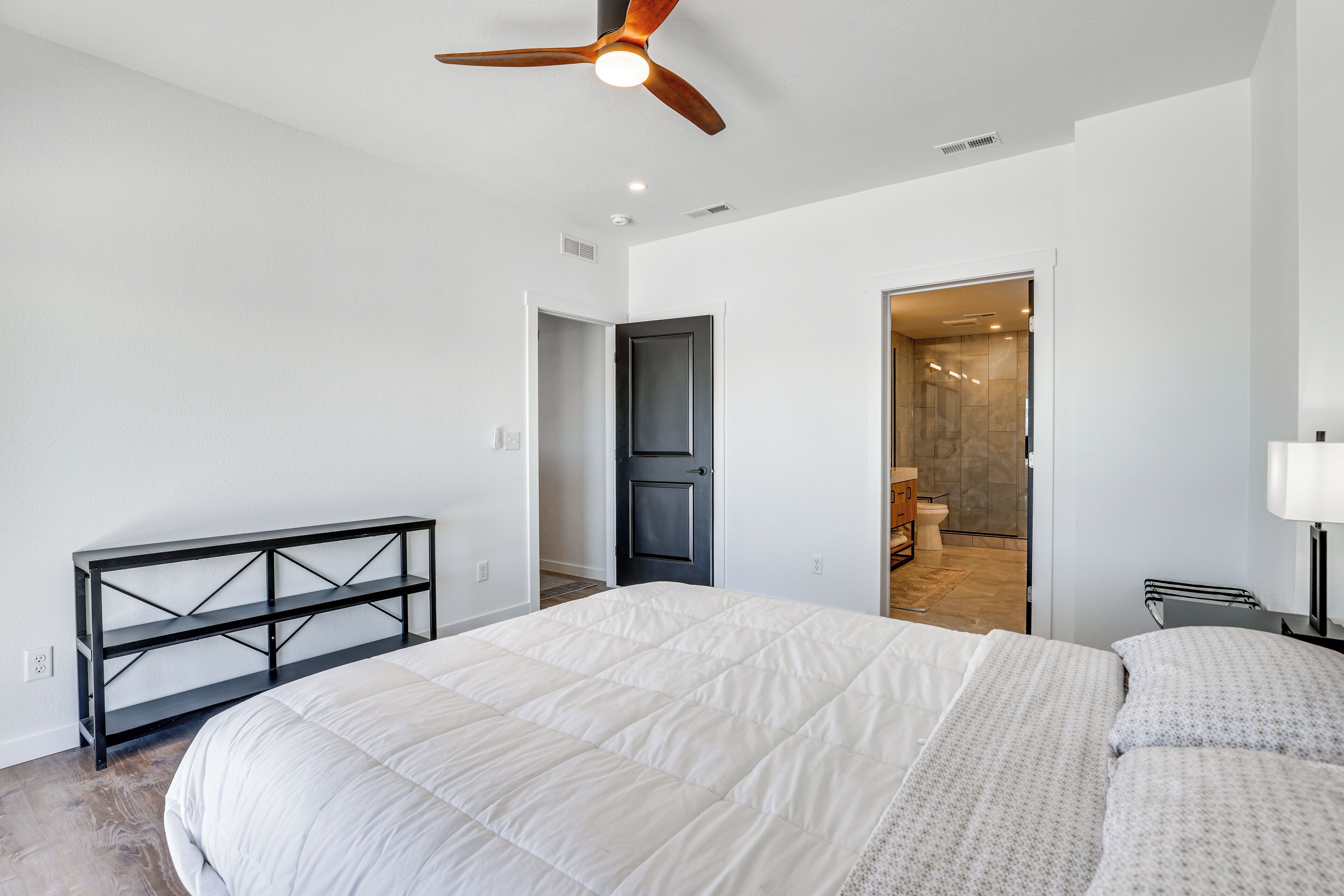 A modern bedroom with a large bed, a ceiling fan, and a bench.