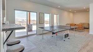 A spacious room with a ping pong table, a sofa, and a view of a mountainous landscape through large windows. - Great for Groups! Luxury Mtn-view Granby Home (Granby)