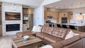 A modern living room with a stone fireplace, leather sofa, and a wooden coffee table. - Great for Groups! Luxury Mtn-view Granby Home (Granby)