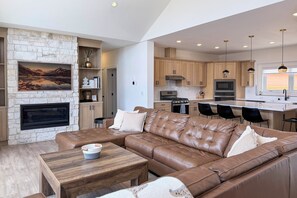 A modern living room with a stone fireplace, leather sofa, and a dining area with wooden cabinets and a kitchen in the background.