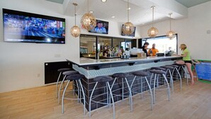 Un área de bar moderna con una barra larga, varios taburetes y lámparas colgantes.