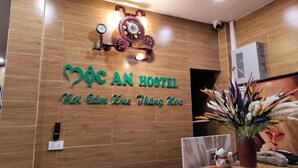 A reception desk with a wooden panel wall, a clock, and a sign that reads "ĐƠC AN HOSTEL". - Moc An by Bay Hotel (Hanoi)