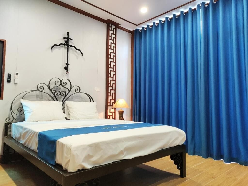 A neatly made bed with white and blue bedding, a decorative wall hanging, and a blue curtain.