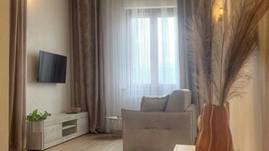 Ein Wohnzimmer mit einer Couch, einem an der Wand montierten Fernseher, einer Pflanze und einer Vase mit Trockenblumen.