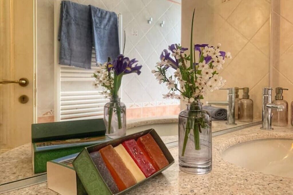 Ein Badezimmer mit Waschbecken, zwei Vasen mit Blumen und einer Schale voller farbiger Seifen.