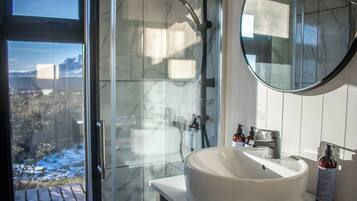 A bathroom with a large window, a white sink, and a shower with a glass door.