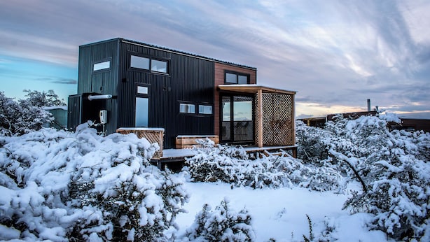 Een modern, tweelaags huis met een groot balkon en een klein, afgesloten portiek, omgeven door met sneeuw bedekte bomen.