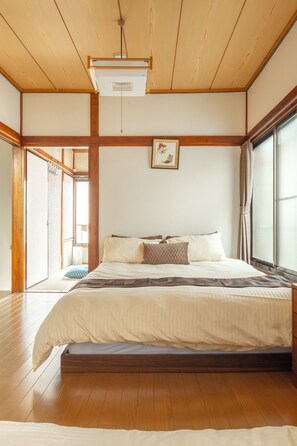 Une chambre de style japonais traditionnel, avec un plafond en bois, un grand lit recouvert de linge de lit blanc et une porte coulissante donnant sur un balcon.