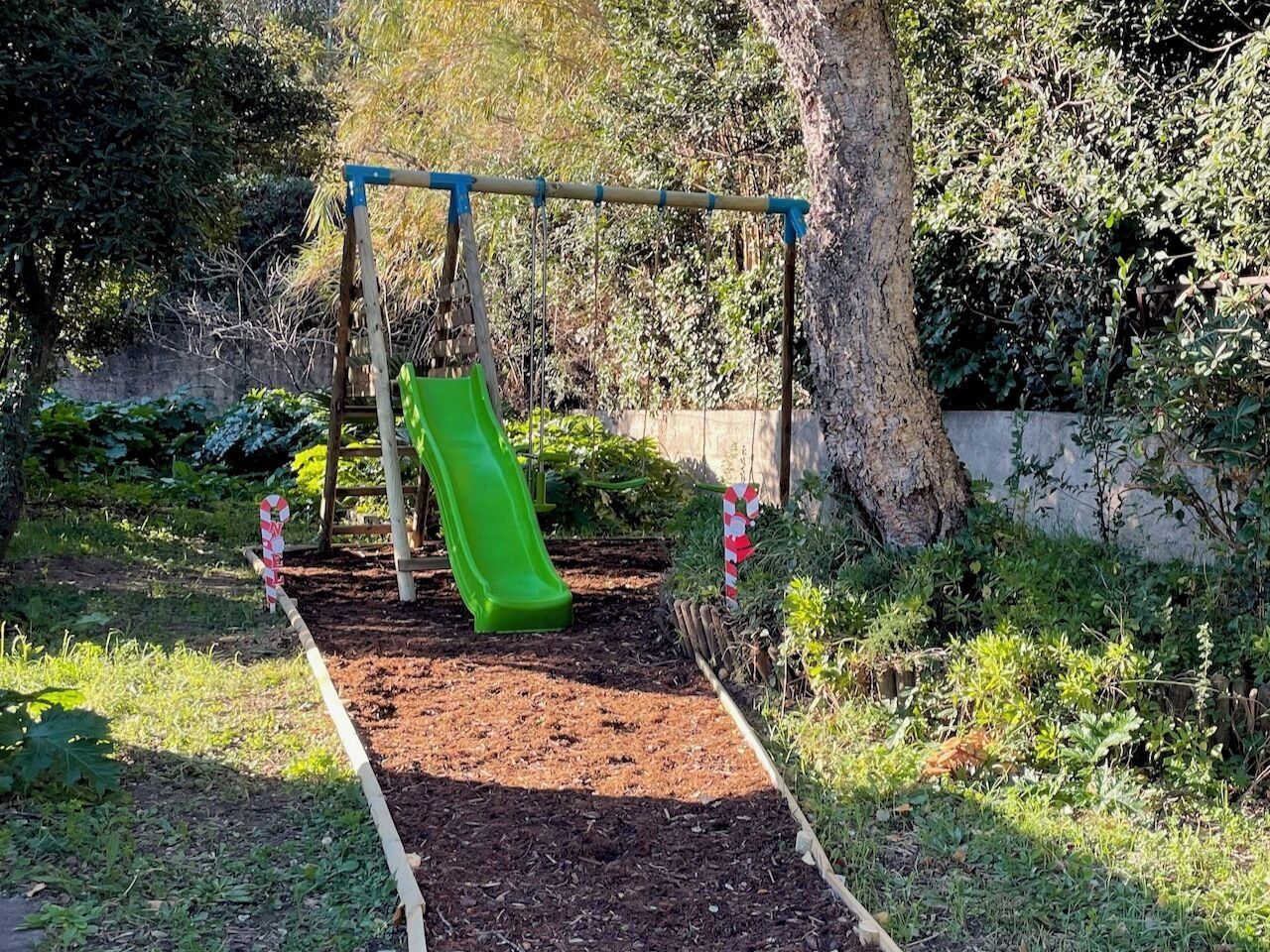 Un parc infantil amb un tobogan verd i un conjunt de cadira de balancí.