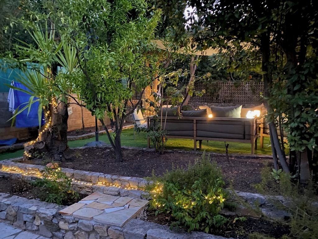 A garden area with a stone pathway, a bench, and string lights.