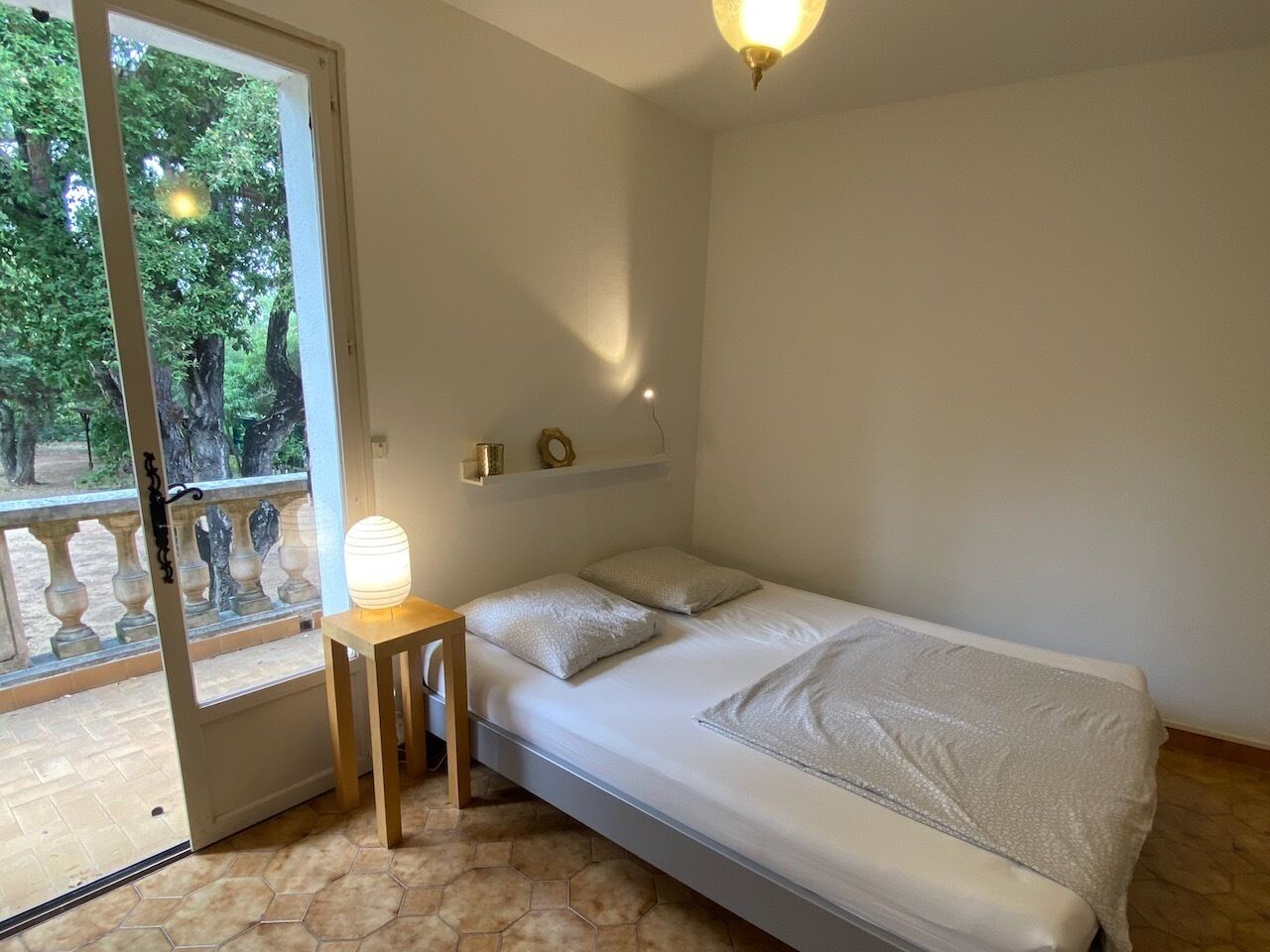 A bedroom with a bed, a bedside table, a lamp, and a view of trees through a glass door.