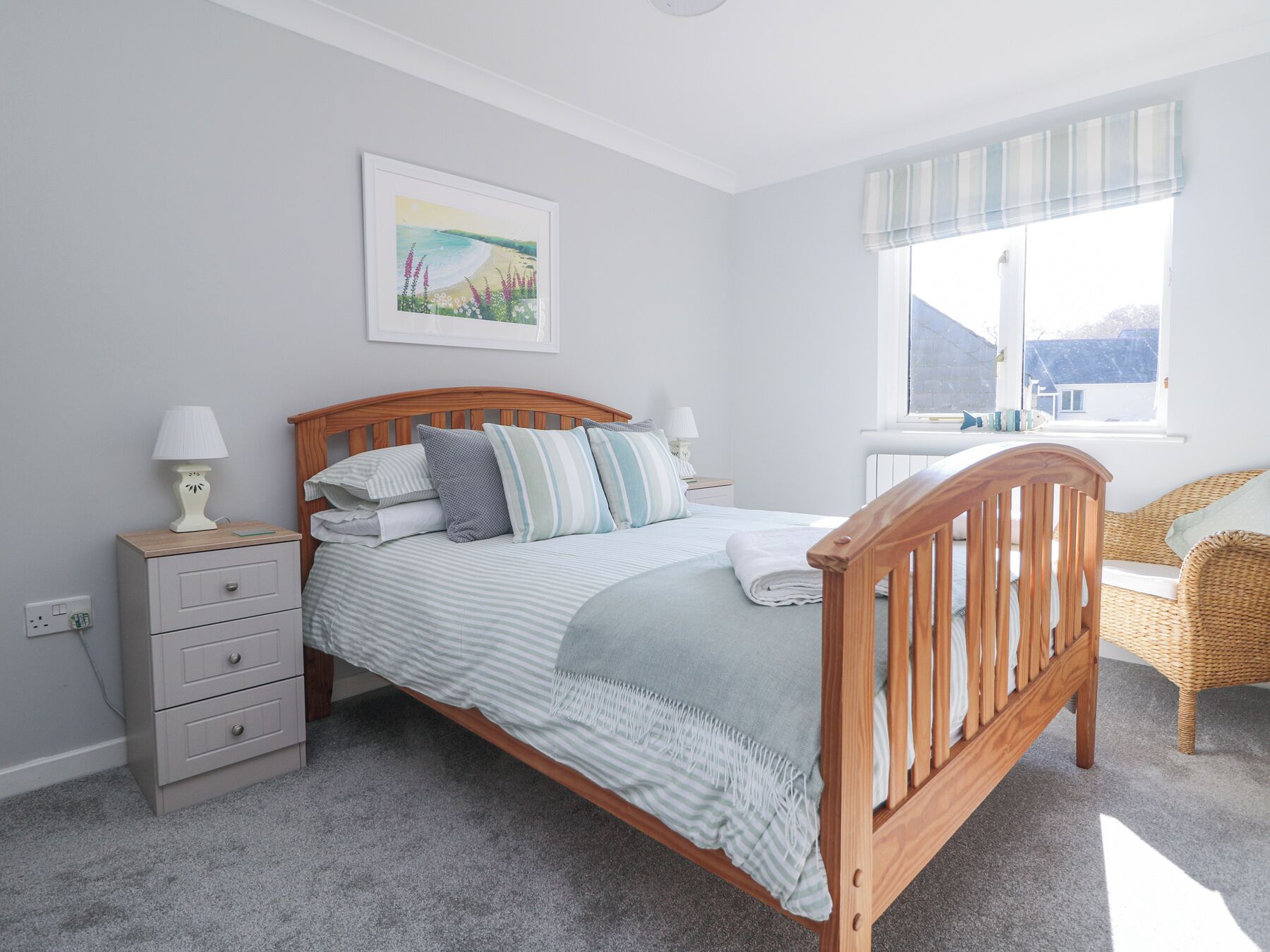 A bedroom with a wooden bed, a bedside table with lamps, a chair, and a window with a view of the outdoors.