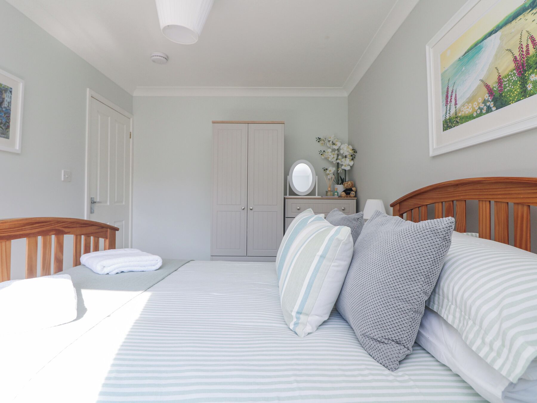 Een slaapkamer met een bed, nachtkastjes, een dressoir, een spiegel en een schilderij aan de muur.