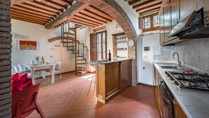 A kitchen with a central island, a dining area with a table and chairs, and a spiral staircase leading to an upper level. - Casa Vecchia, Montebuoni, Gaiole in Chianti, Siena and Chianti (Gaiole in Chianti)