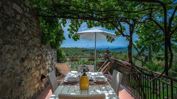 An outdoor dining area with a stone wall, wicker furniture, and a table set for two. - Casa Vecchia, Montebuoni, Gaiole in Chianti, Siena and Chianti (Gaiole in Chianti)