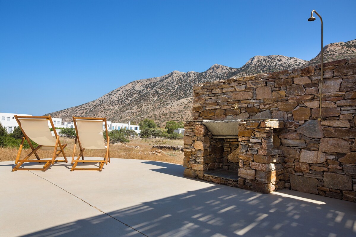 A stone fireplace, two wooden lounge chairs, and a clear view of a mountainous landscape.