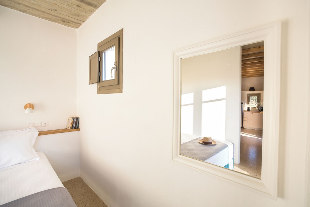 A bedroom with a bed, a bedside table, a mirror, and a window.