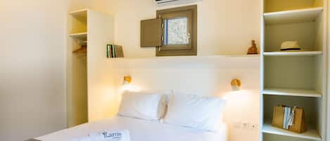 A hotel room with a bed, a wardrobe, a shelf with books, and an air conditioning unit.