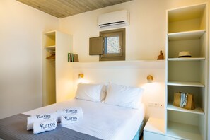 A hotel room with a bed, a wardrobe, a small window, and a shelf with a hat and a bag.