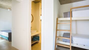 Un dormitorio con una cama litera, un baño pequeño con lavamanos y un armario con estantes.