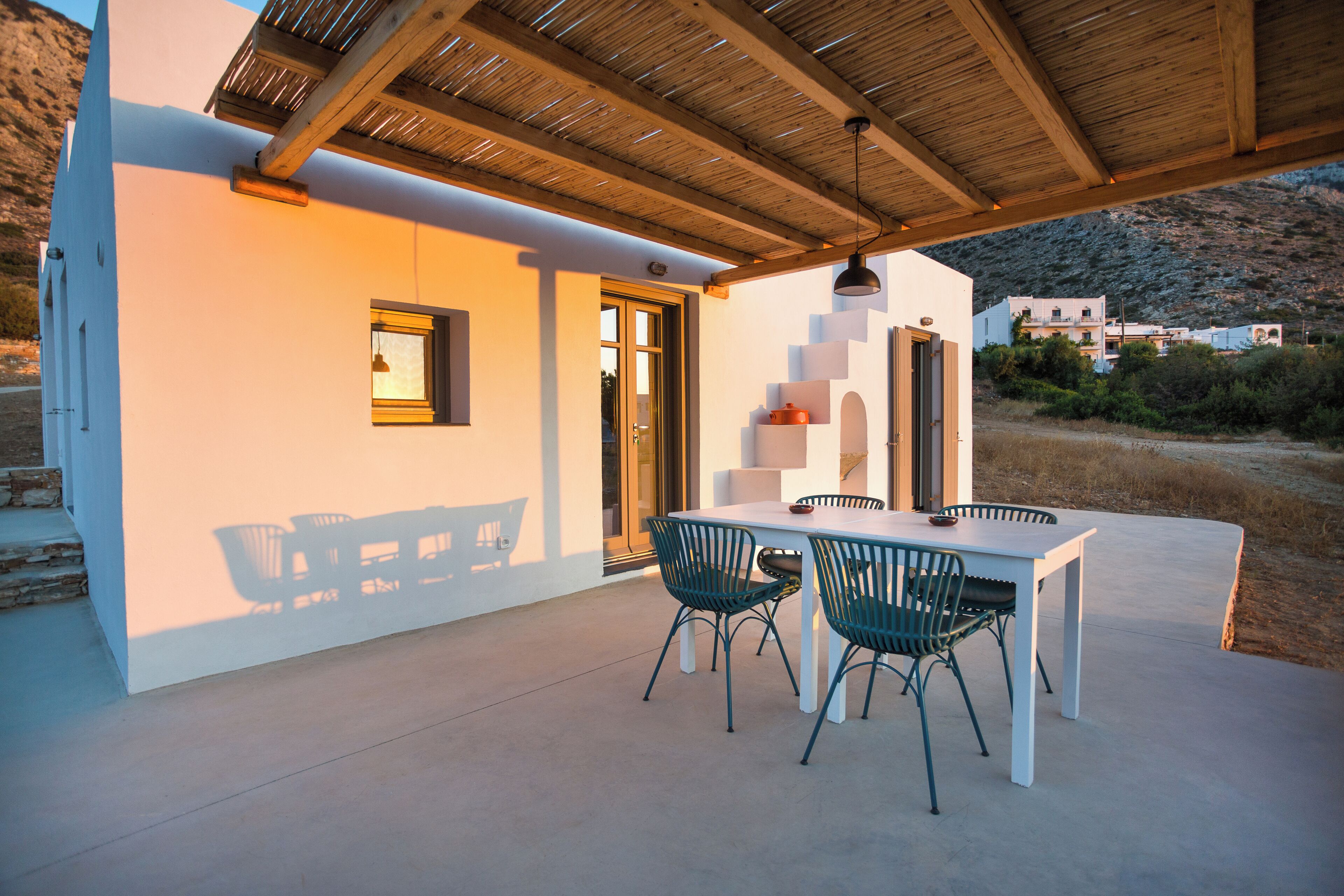 Un patio techado con una mesa blanca y sillas verdes, techo de madera y vistas del paisaje circundante.