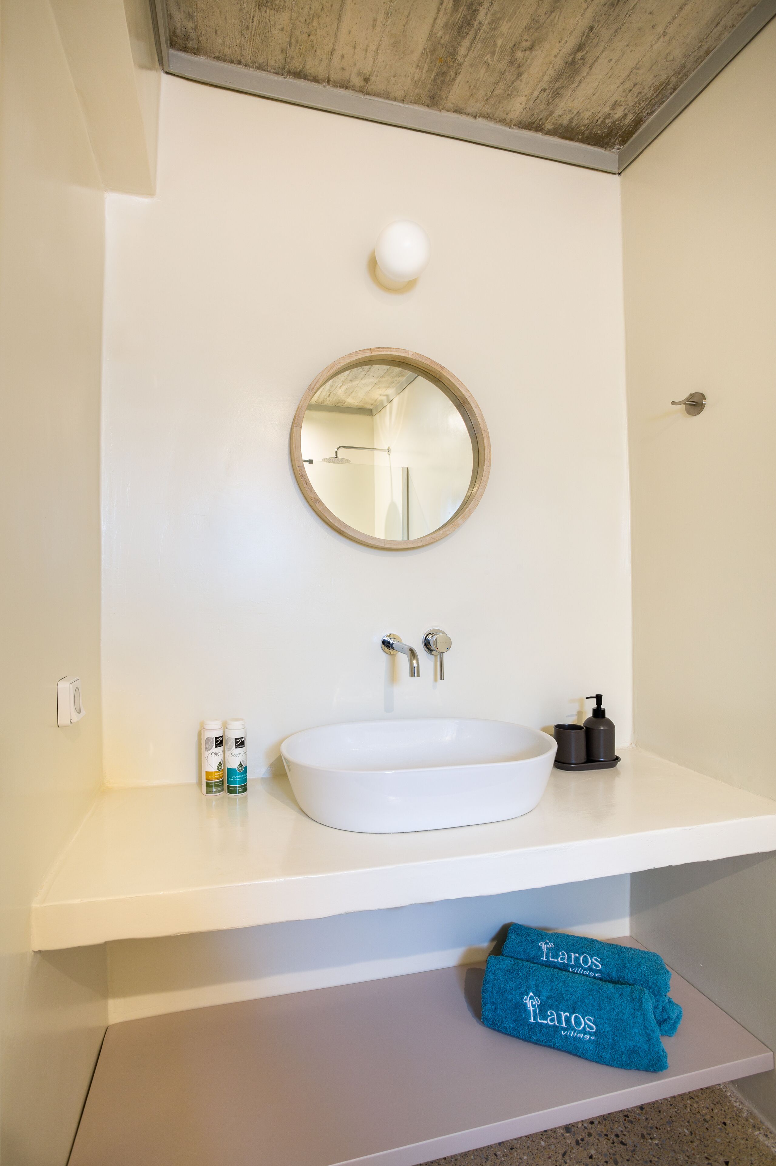 Un baño con un lavamanos blanco, un espejo redondo y un perchero con toallas.