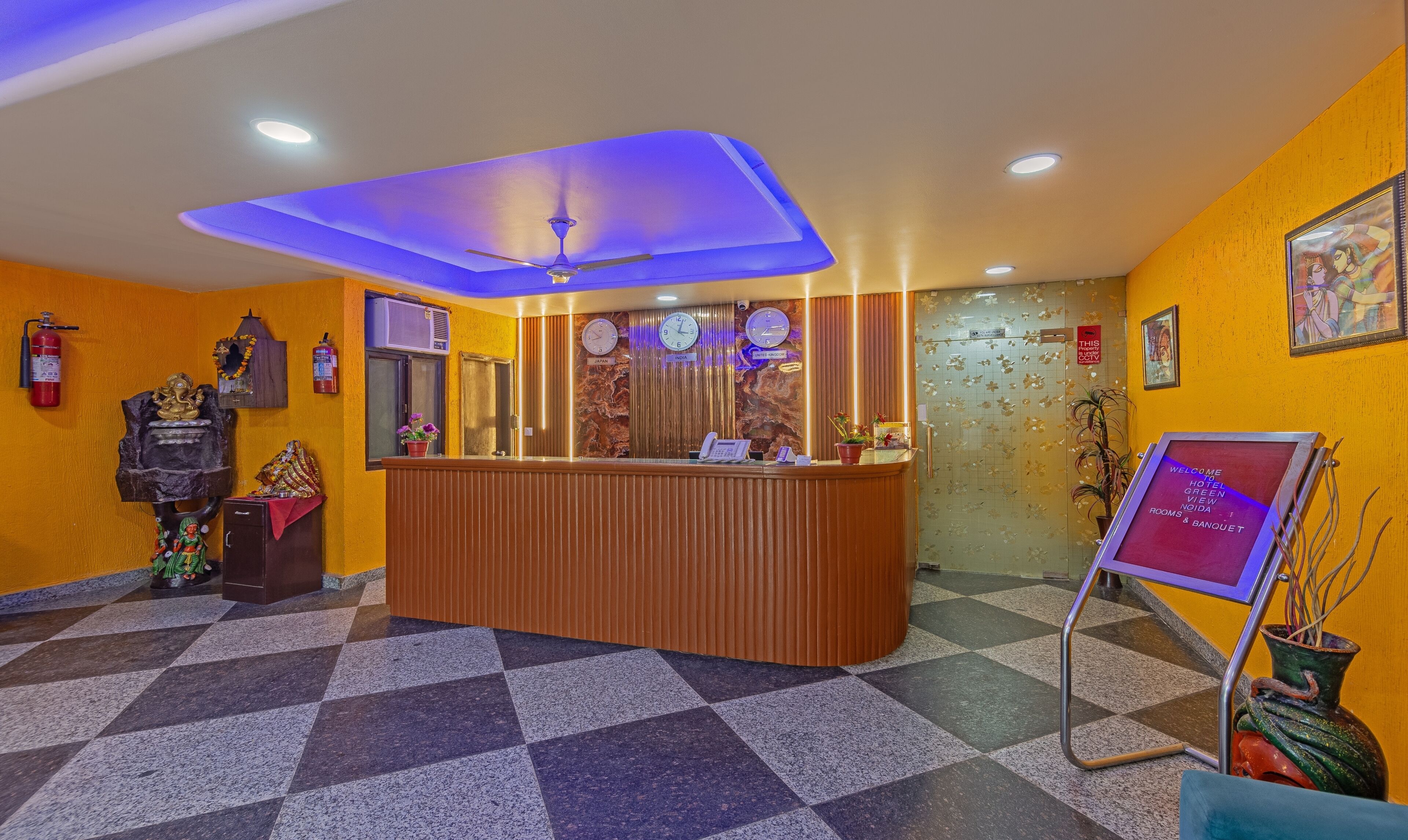 A hotel reception area with a check-in counter, a clock, and a fire extinguisher on the wall.