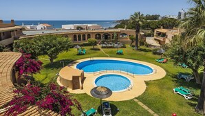 Una piscina con vista al océano, rodeada de palmeras y sillones de descanso.