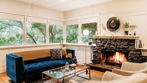 A living room with a blue sofa, a glass coffee table, and a stone fireplace. - Luxury Treetop Escape with a Garden glasshouse (Kalorama)