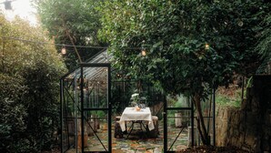 A glass-enclosed outdoor dining area with a stone pathway leading to a table set with a white tablecloth and a vase of flowers. - Luxury Treetop Escape with a Garden glasshouse (Kalorama)