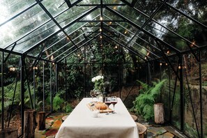 A greenhouse with a table set for a meal, surrounded by greenery and a glass ceiling. - Luxury Treetop Escape with a Garden glasshouse (Kalorama)