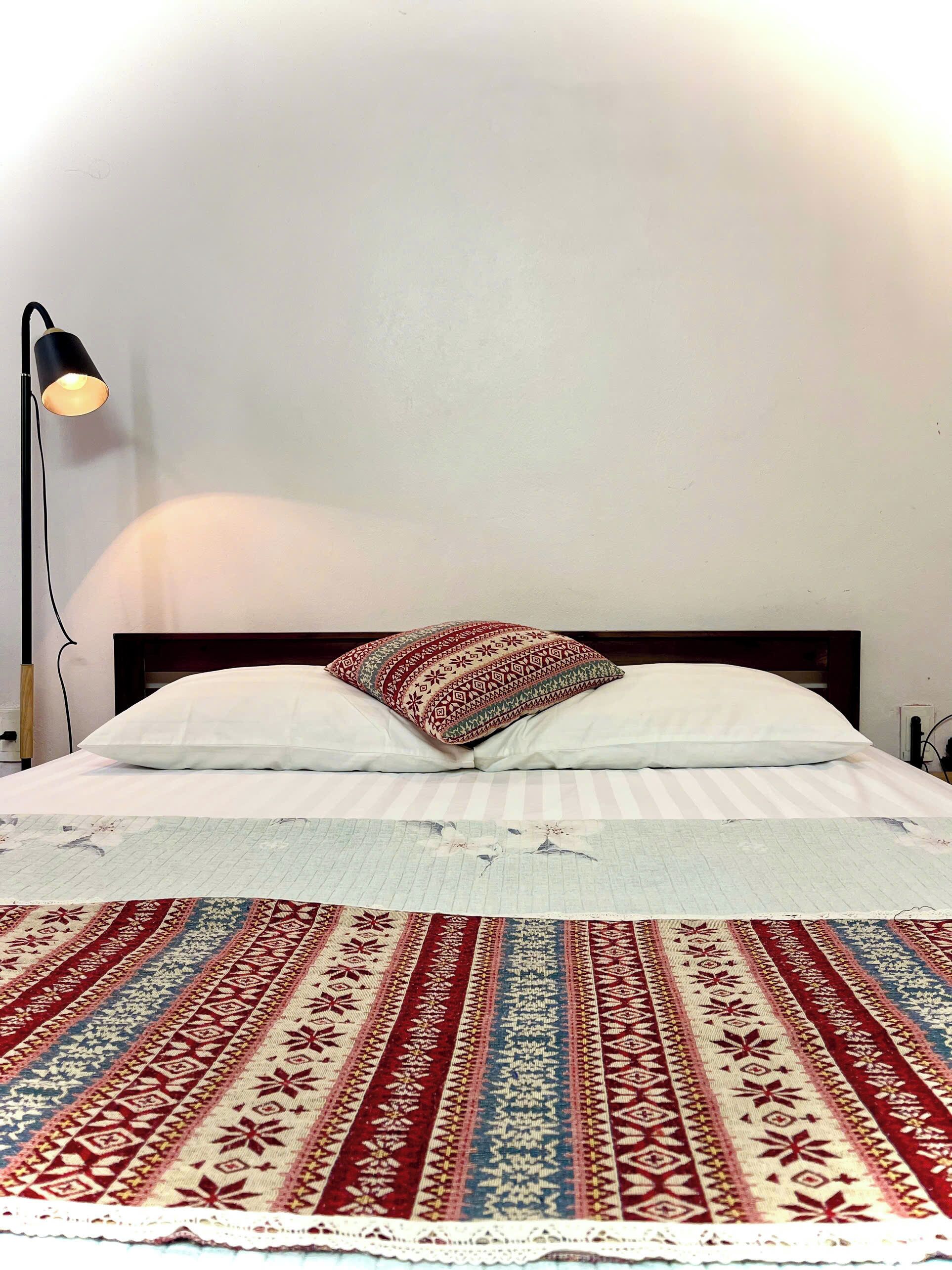 A bed with a patterned bedspread, two pillows, and a bedside lamp.
