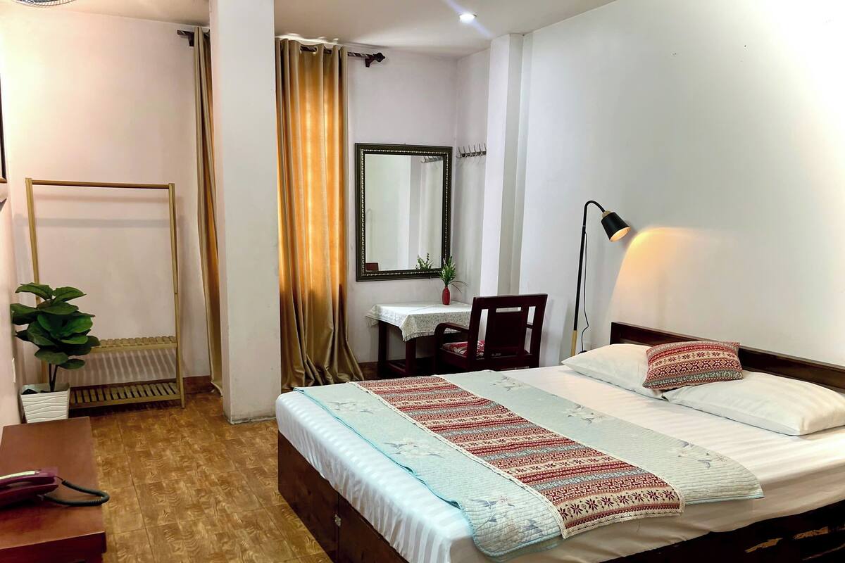 A neatly arranged bedroom with a bed, bedside table, lamp, and a small desk with chair.