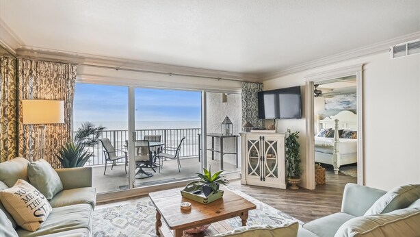 Un vaste espace de vie avec un balcon donnant sur la mer, un téléviseur fixé au mur et un coin salon confortable.