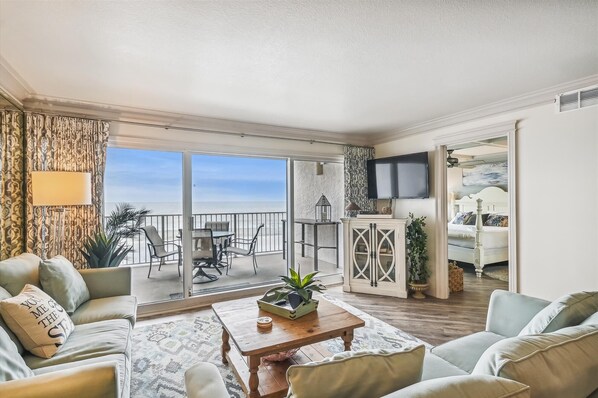 Relax in a spacious living area with ocean views through large sliding glass doors, featuring a comfortable seating area and a modern aesthetic.