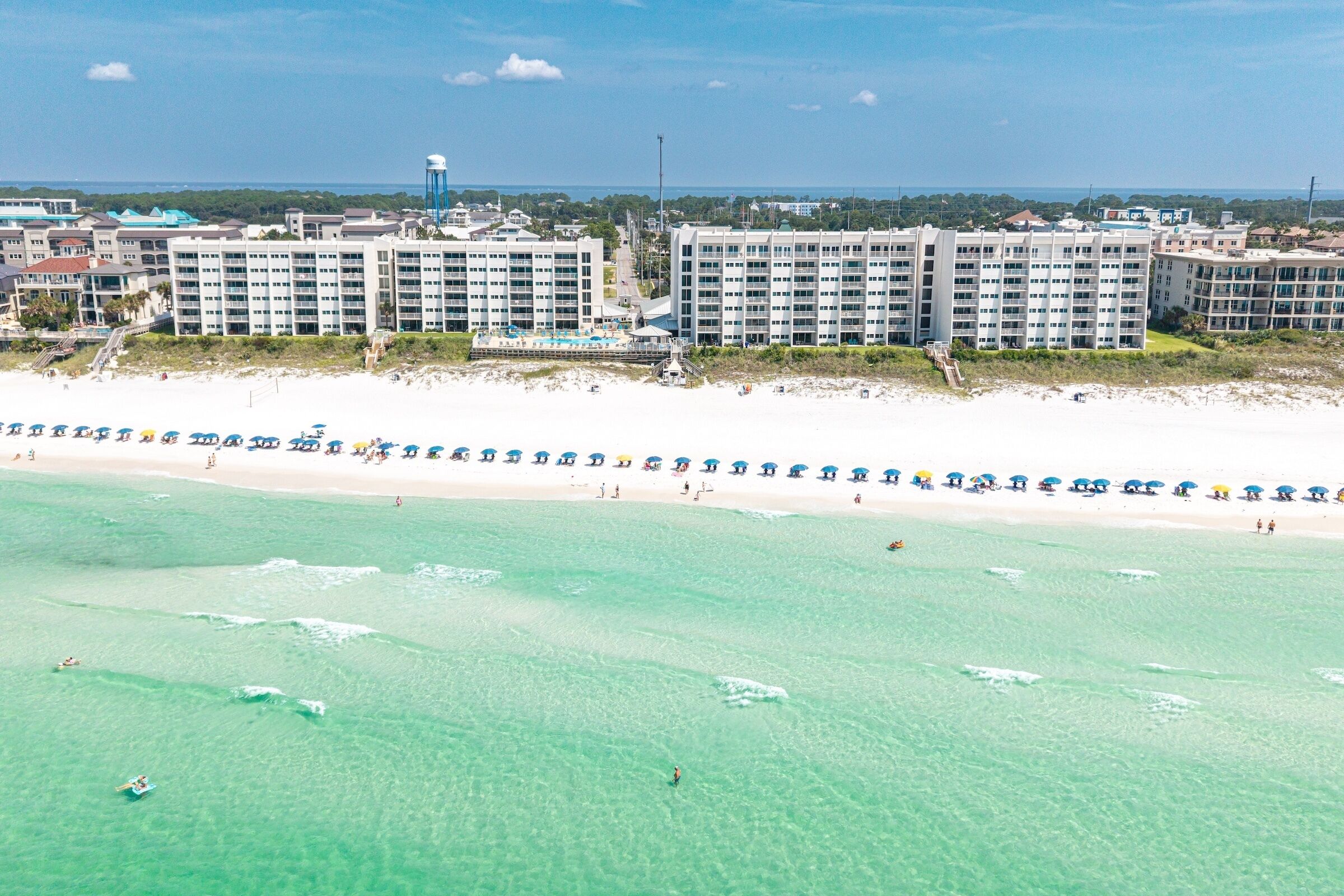 Een hotel aan het strand met meerdere gebouwen, een zandstrand en helder turquoise water.
