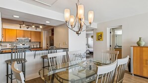 A modern kitchen with wooden cabinets, a stainless steel stove, and a glass dining table with white chairs. - Beach House 303B is Beautiful Gulf Front 2 BR with Free Beach Service for 2 (Miramar Beach)